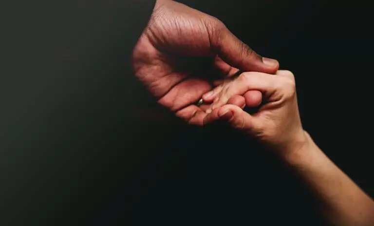A black male hand reaching down for a white female hand to lift her up in support