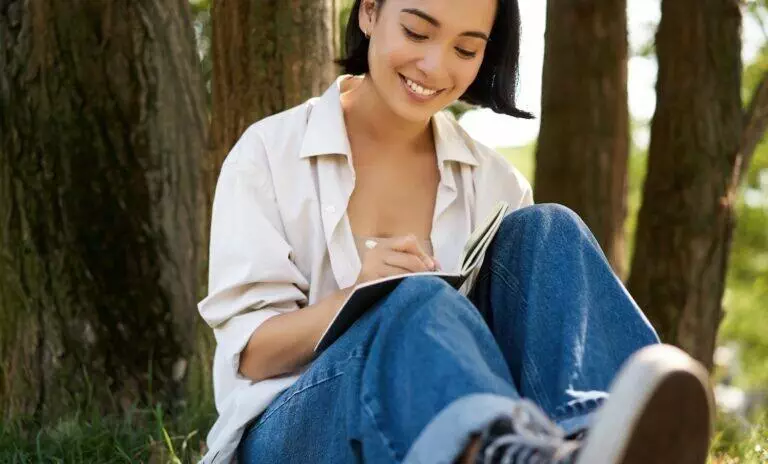 Portrait of happy asian girl sitting in park and writing in her journal
