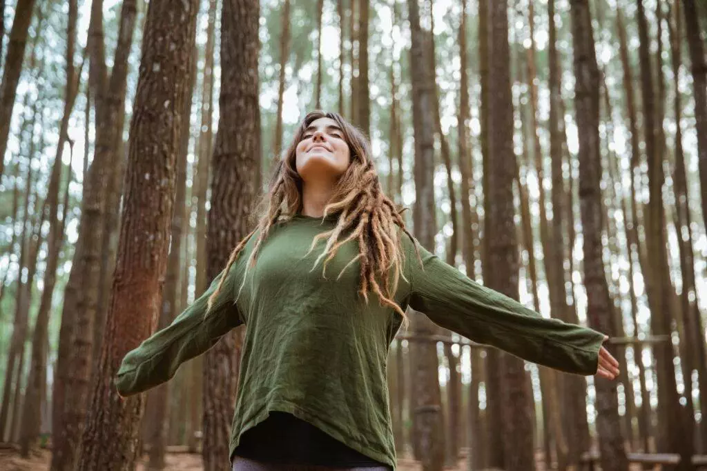 woman in green sweatshirt standing alone with trees behind her