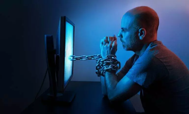 man chained to a computer monitor. internet addiction concept