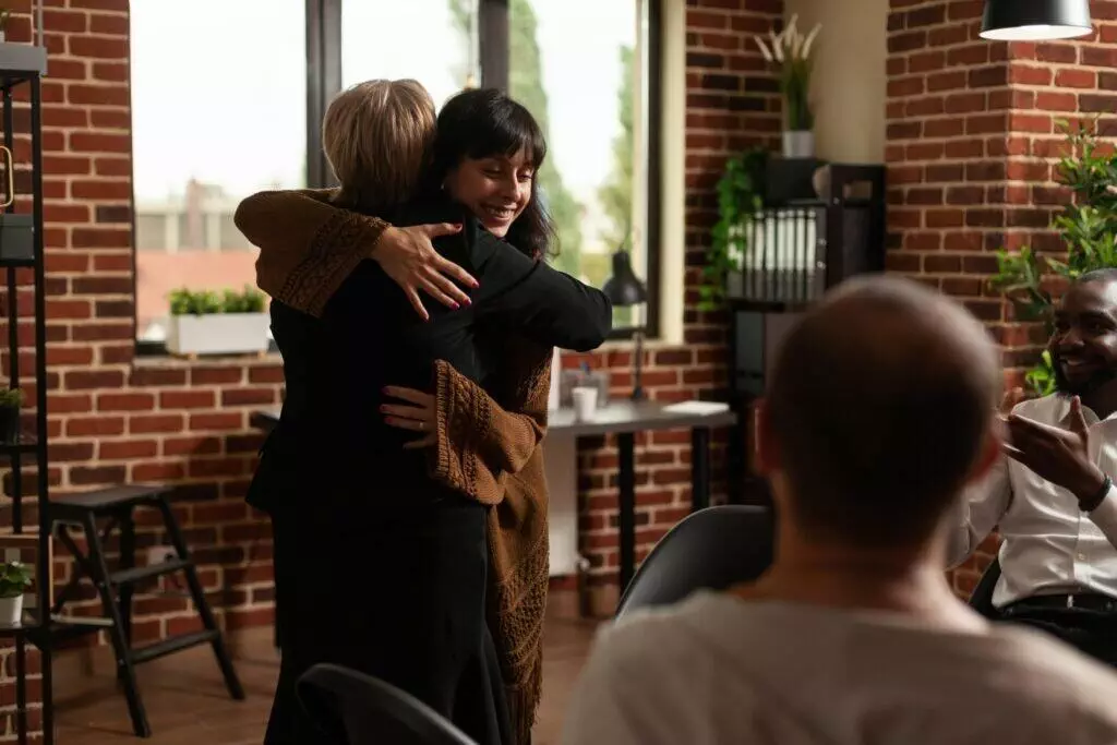 Woman and therapist hugging after sharing recovery progress with aa meeting group