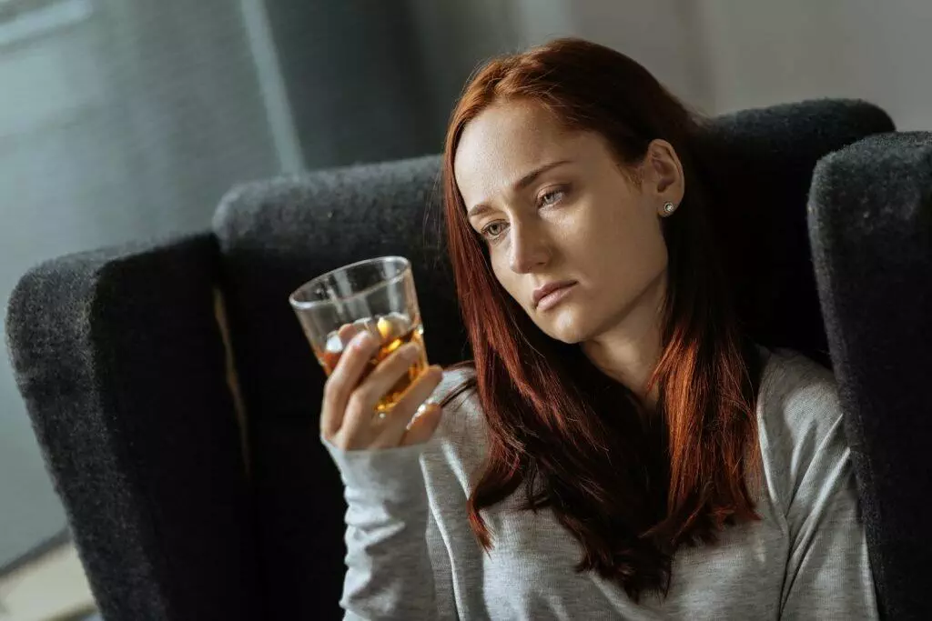 depressed woman looking at a glass of alcohol in her hand