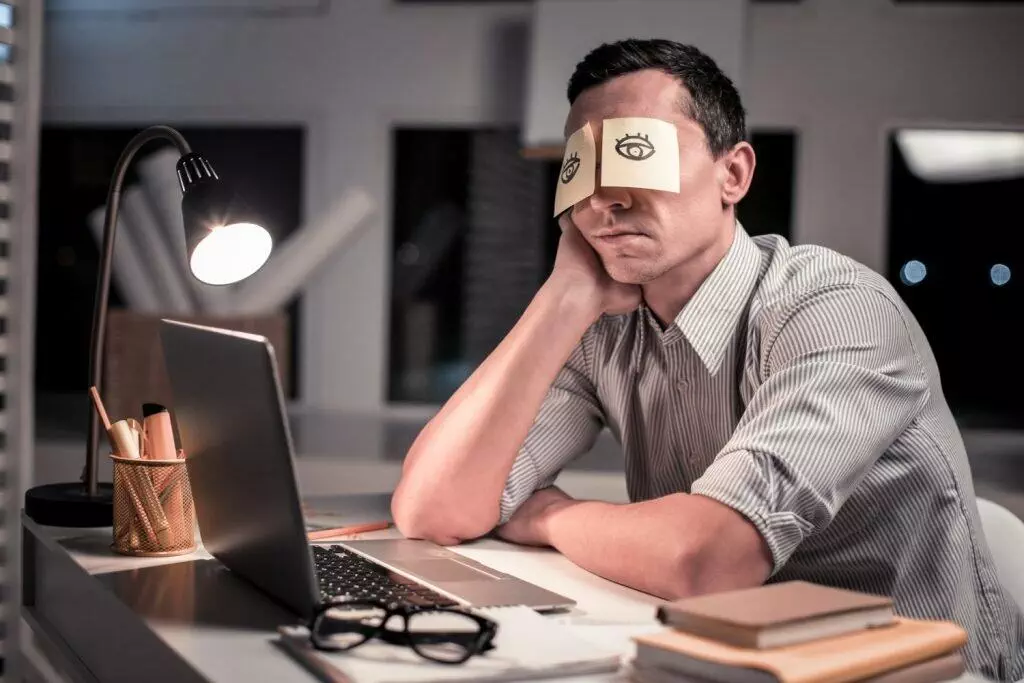tired man on desk with paper stuck in eyes